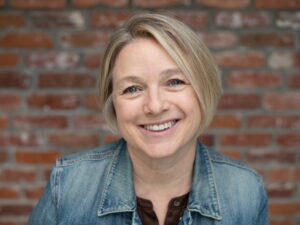 Poet Patrica Caspers, wearing denim jacket against brick background